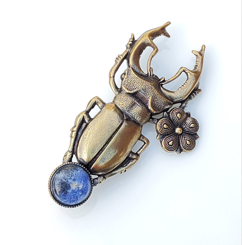 broche scarabée en laiton avec une patine noire pour plus de relief, une matière plus riche. Il enserre entre ses pattes un cabochon bleu en sodalite. C'est la version esprit vintage de ce joli scarabée broche. 4,5 cm de long environ sur 2,5 cm de large environ.